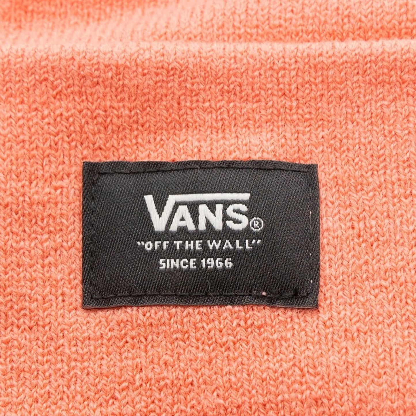 Close-up of a black Vans label on a coral-colored polyester winter beanie hat for unisex use.